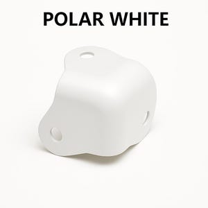 May include: A white corner protector with three holes, labeled "POLAR WHITE" in bold, black text. The rounded design is made of a smooth, solid material, ideal for furniture or home decor.