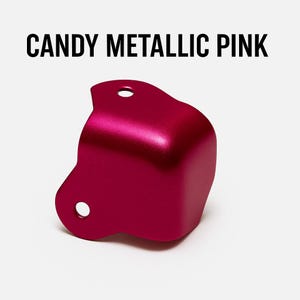 May include: A metallic pink corner protector with rounded edges and two holes on each side.  CANDY METALLIC PINK is written in black text above the corner protector.