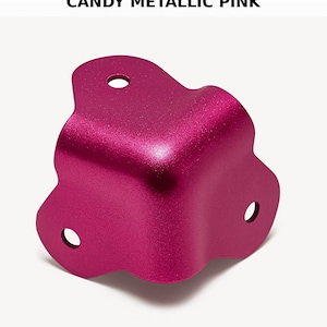 May include: A metallic pink corner brace with rounded edges and three holes. The brace is made of metal and has a shiny finish.