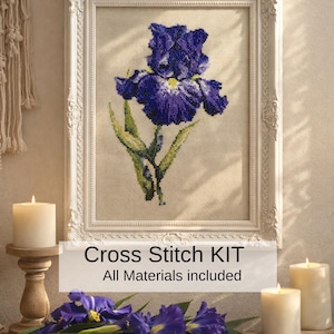 Può includere: Un kit a punto croce incorniciato con un vibrante fiore di iris viola. L'opera d'arte è ambientata su uno sfondo neutro all'interno di una cornice bianca ornata. Il testo "Cross Stitch KIT All Materials included" è visualizzato sotto.