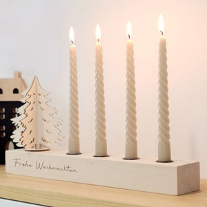 Può includere: Un portacandele in legno con quattro candele bianche, un albero di Natale in legno ritagliato e il testo "Frohe Weihnachten" sul davanti.