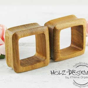 Op de afbeelding: Twee vierkante oorstekers van hout, elk met een gladde, natuurlijke houten afwerking. De stekers zijn handgemaakt en hebben een vierkante opening in het midden.
