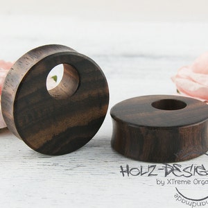 May include: Two dark brown wooden ear gauges with a smooth, polished finish. The gauges are round with a hole in the center. The gauges are made of wood and have a natural grain pattern.