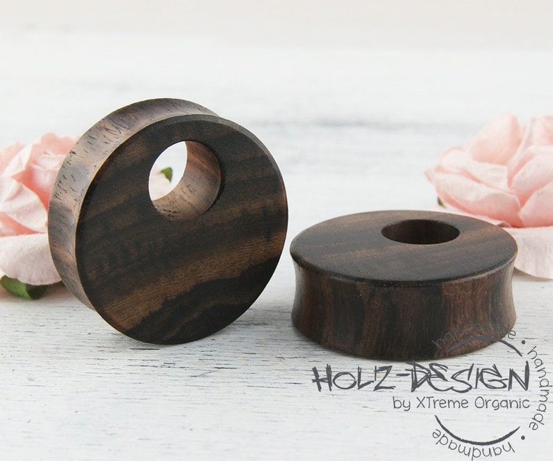 May include: Two dark brown wooden ear gauges with a smooth, polished finish. The gauges are round with a hole in the center. The gauges are made of wood and have a natural grain pattern.