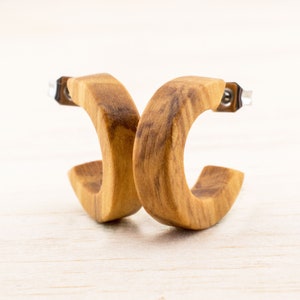 Könnte beinhalten: Ein Paar Holz-Creolen mit einer natürlichen Holzmaserung. Die Ohrringe sind aus Olivenholz gefertigt und haben einen silberfarbenen Metallstift.