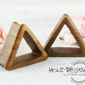 Op de afbeelding: Twee houten oorpluggen in de vorm van een driehoek. De pluggen zijn bruin en hebben een gladde afwerking. De pluggen zijn handgemaakt door Holz-Design by X-Treme Organic.