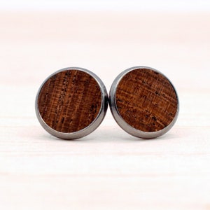 May include: A pair of round wood earrings with a silver metal rim. The wood has a dark brown color and a natural wood grain pattern.