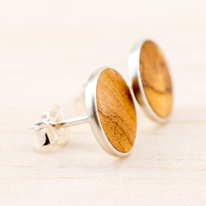 Op de afbeelding: Een paar ronde houten oorbellen met zilveren instellingen. Het hout is lichtbruin van kleur met donkerbruine strepen.