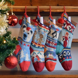 May include: Five colorful knitted Christmas stockings with names written on tags. The stockings are hanging on a wooden shelf with a Christmas tree in the background.