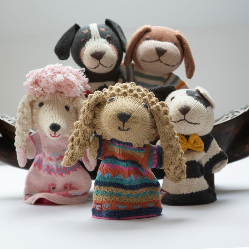 Pu&ograve; includere: Cinque marionette di cane a maglia, ognuna con un design e un colore diversi. Le marionette sono fatte di filato morbido e hanno espressioni facciali. Sono disposte in fila, con la marionetta pi&ugrave; grande al centro.