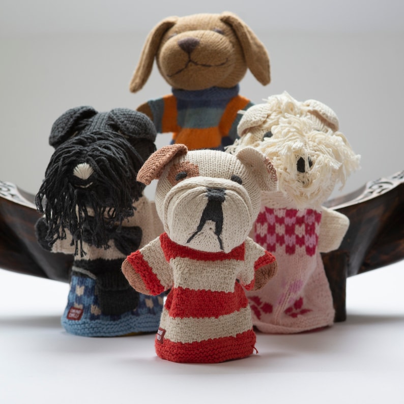 Pu&ograve; includere: Quattro marionette per dita a forma di cane in maglia. Le marionette sono di colore marrone, nero, bianco e crema con strisce rosso e bianco, strisce rosa e bianco e strisce blu e bianco.