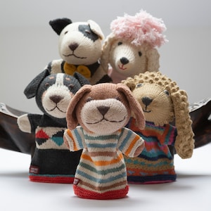 Pu&ograve; includere: Cinque marionette per dita a maglia, ognuna raffigura un animale diverso. Le marionette sono un cane bianco e nero, un cane marrone e bianco, un cane marrone, un cane marrone e un barboncino bianco con un fiocco rosa. Le marionette sono tutte sorridenti e hanno occhi grandi ed espressivi.