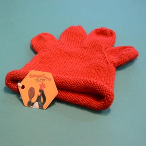 Puede incluir: Un gorro de punto rojo brillante con un diseño único en forma de mano. El gorro tiene un borde enrollado y una etiqueta con el texto "Wallace & Gromit Est. 1959" y una imagen de dibujos animados. El gorro está hecho de un hilo grueso y texturizado.