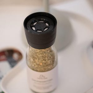 K&ouml;nnte beinhalten: Eine Glasflasche gef&uuml;llt mit getrockneten Kr&auml;utern und Gew&uuml;rzen, mit einem schwarzen Schraubverschluss. Der Deckel hat eine kleine, runde, schwarze L&uuml;ftung in der Mitte.