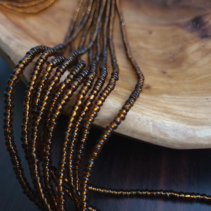 May include: A close-up of a strand of brown glass beads. The beads are small and round, and they are strung together on a thin wire. The beads are arranged in a loose, flowing pattern.