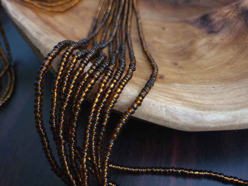 May include: A close-up of a strand of brown glass beads. The beads are small and round, and they are strung together on a thin wire. The beads are arranged in a loose, flowing pattern.