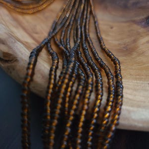 May include: A close-up of a strand of brown and gold beads. The beads are small and round, and they are arranged in a long, flowing strand. The strand is lying on a wooden surface.