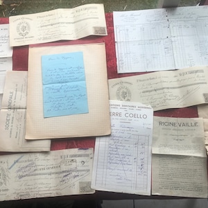 May include: A collection of vintage documents, including handwritten letters, receipts, and invoices, are arranged on a red surface. The papers vary in size and shape, with some featuring stamps and handwritten notes. A blue note is centered.