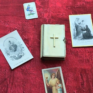 May include: A collection of religious imagery, including a small white book with a cross on the cover, a card with a cross and a heart, and a card with a depiction of the Virgin Mary and a child.