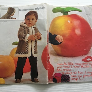 May include: A vintage magazine spread featuring a child modeling a brown and cream-colored hooded coat. The coat has a textured knit design with a cream-colored trim. The magazine also features a large apple prop.