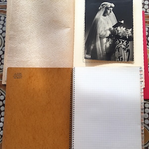 May include: An open vintage scrapbook with a black and white photograph of a person in a veil holding flowers. The scrapbook includes lined and blank pages, and a spiral binding. The text "LA BELLE REVISTUDIE" is visible.