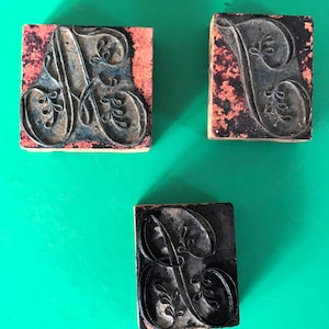 May include: Three vintage wooden letterpress blocks with the letters A, B, and C carved in a decorative script font. The blocks are made of wood and have a dark brown finish. The letters are raised and have a slightly worn look.