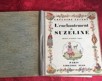 May include: A vintage children's book titled "L'enchantement de Suzeline" by Grégoire Leclos with illustrations by Albert Uriet. The cover features a colorful floral border and a scene of a young girl in a pink dress and apron standing in a field with a goat.