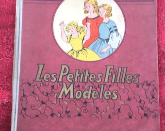 May include: Vintage book cover with the title "Les Petites Filles Modèles" in gold lettering. The cover is a deep red color and features an illustration of three girls in a circular frame. The author's name is also printed on the cover.