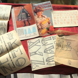 May include: A collection of vintage embroidery patterns featuring alphabets, birds, and floral designs. The patterns are printed on cream-colored paper with black ink. The patterns are titled "Les plus beaux Tricots Special" and "L'Oiseau Sigarle" and "Blanches Paquerettes".