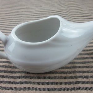 Peut inclure: Une poire en céramique blanche pour lavement, avec une surface lisse et arrondie. La poire est conçue pour un usage médical.