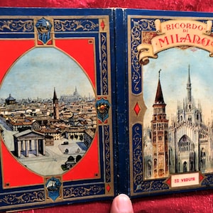 Peut inclure: Un livret souvenir vintage avec deux pages illustrées. La page de gauche présente un paysage urbain dans un cadre orné rouge et bleu. La page de droite affiche une cathédrale et une tour avec le texte "RICORDO DI MILANO" et "32 VEDUTE".