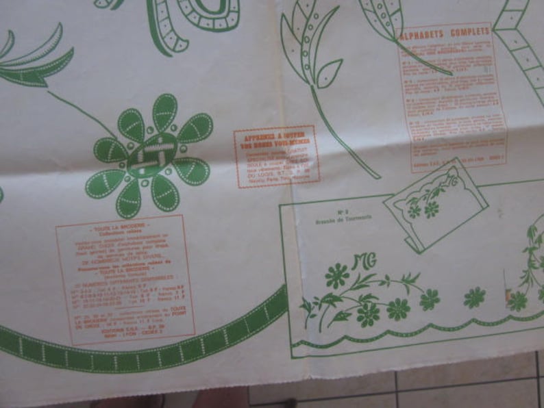 May include: A white sheet of paper with a green and white floral design. The paper has instructions for embroidery, including a section titled "Alphabets Complet." The paper also has a section titled "Apprenez a broder vos motifs" with instructions in French.