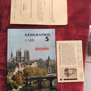 Peut inclure: Une couverture de livre scolaire vintage pour une classe de géographie de 3ème. La couverture présente une photographie couleur de la Seine et de la cathédrale Notre-Dame à Paris, France. Le livre est intitulé "Géographie 3e" et est publié par Librairie Hachette.