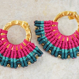 May include: A pair of gold hoop earrings with a pink and teal macrame design. The hoops are hammered and have a textured finish.