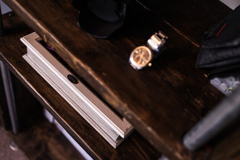May include: A close-up shot of a dark brown wooden shelf with a level, watch, and other accessories. The level is light gray with a black oval label. The watch has a gold face and a silver band. A black cap and a black leather case are also visible.