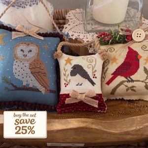 Può includere: Tre cuscini decorativi ricamati con temi naturali. Uno presenta un gufo su sfondo blu, un altro un uccello nero e il terzo un cardinale rosso. Ogni cuscino ha un design unico ed è impreziosito da fiocchi e frange.