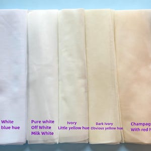 May include: A display of fabric swatches in various shades of white and off-white, including cold white, pure white, ivory, and champagne. Each swatch is labeled with its color description, such as "with blue hue" or "with red hue."