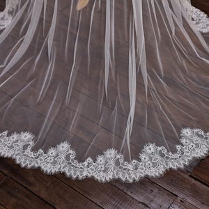 May include: A sheer white wedding veil with a delicate, scalloped lace trim. The veil is made of a lightweight fabric that drapes gracefully. The lace trim features an intricate floral design, adding a touch of elegance to the bridal accessory.