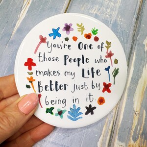 May include: White round ceramic coaster with colorful painted flowers and the text "You're One of those People who makes my Life Better just by being in it."