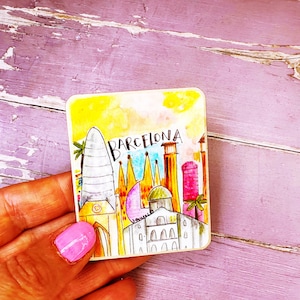 May include: A colourful illustration of the Barcelona skyline, featuring iconic buildings such as the Sagrada Familia and the Agbar Tower. The illustration is painted in a watercolour style with a yellow background and blue sky.