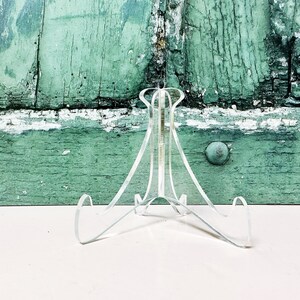 May include: A clear acrylic display stand with three legs. The stand is designed to hold a plate or other flat object.