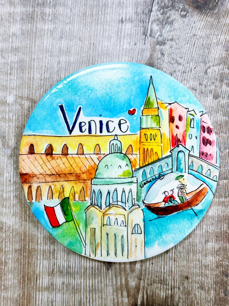 May include: A round, colorful magnet with a watercolor painting of Venice, Italy. The magnet features a gondola with two people, a tall building with a red roof, and the word "Venice" written in black.