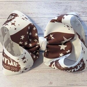 May include: A white and brown ribbon bow with a white star and snowflake pattern. The bow has the text "Girl Scout Brownie" and "1200p 1235" printed on it.