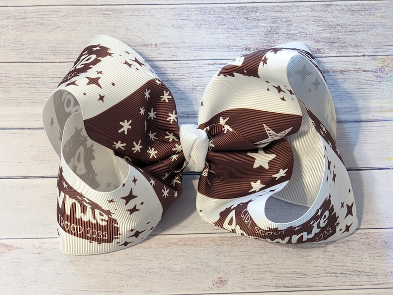 May include: A white and brown ribbon bow with a white star and snowflake pattern. The bow has the text "Girl Scout Brownie" and "1200p 1235" printed on it.