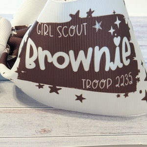 May include: White and brown Girl Scout Brownie troop bow with stars and the text "Girl Scout Brownie Troop 2235".
