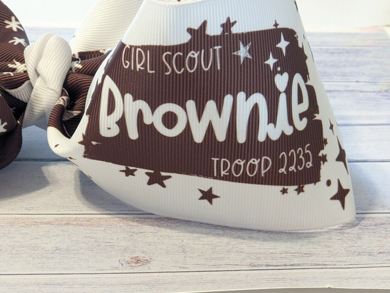 May include: White and brown Girl Scout Brownie troop bow with stars and the text "Girl Scout Brownie Troop 2235".