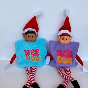 May include: Two elf dolls with red and white hats, striped legs, and black shoes. One doll has a light blue square body with pink and orange text reading NEE DOH. The other doll has a purple square body with pink and orange text reading NEE DOH.