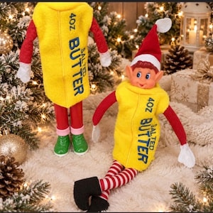 May include: Two elf dolls wearing yellow felt outfits designed to look like sticks of 4oz salted butter. The dolls have red sleeves, white cuffs, and red and white striped legs. One doll wears green shoes, while the other wears black shoes and a red Santa hat.
