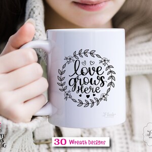 K&ouml;nnte beinhalten: Eine wei&szlig;e Keramiktasse mit einem schwarzen floralen Kranzdesign und dem Text "love grows here".
