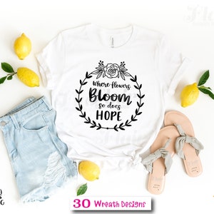 K&ouml;nnte beinhalten: Wei&szlig;es T-Shirt mit einem schwarzen Kranz-Design, auf dem "Wo Blumen bl&uuml;hen, bl&uuml;ht auch Hoffnung" steht.